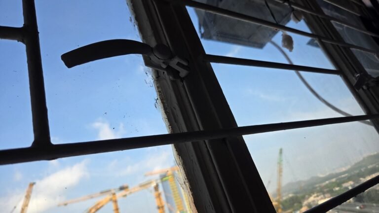 香港舊式鐵窗手柄與窗框近景,窗外可見工地吊機