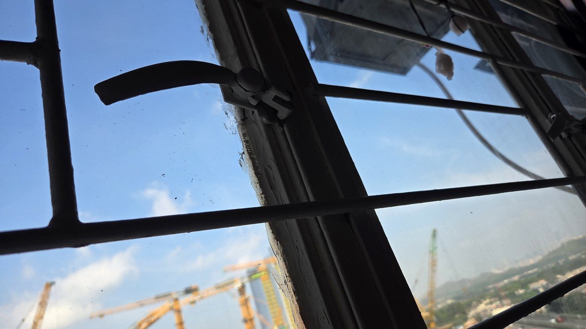 香港舊式鐵窗手柄與窗框近景，窗外可見工地吊機